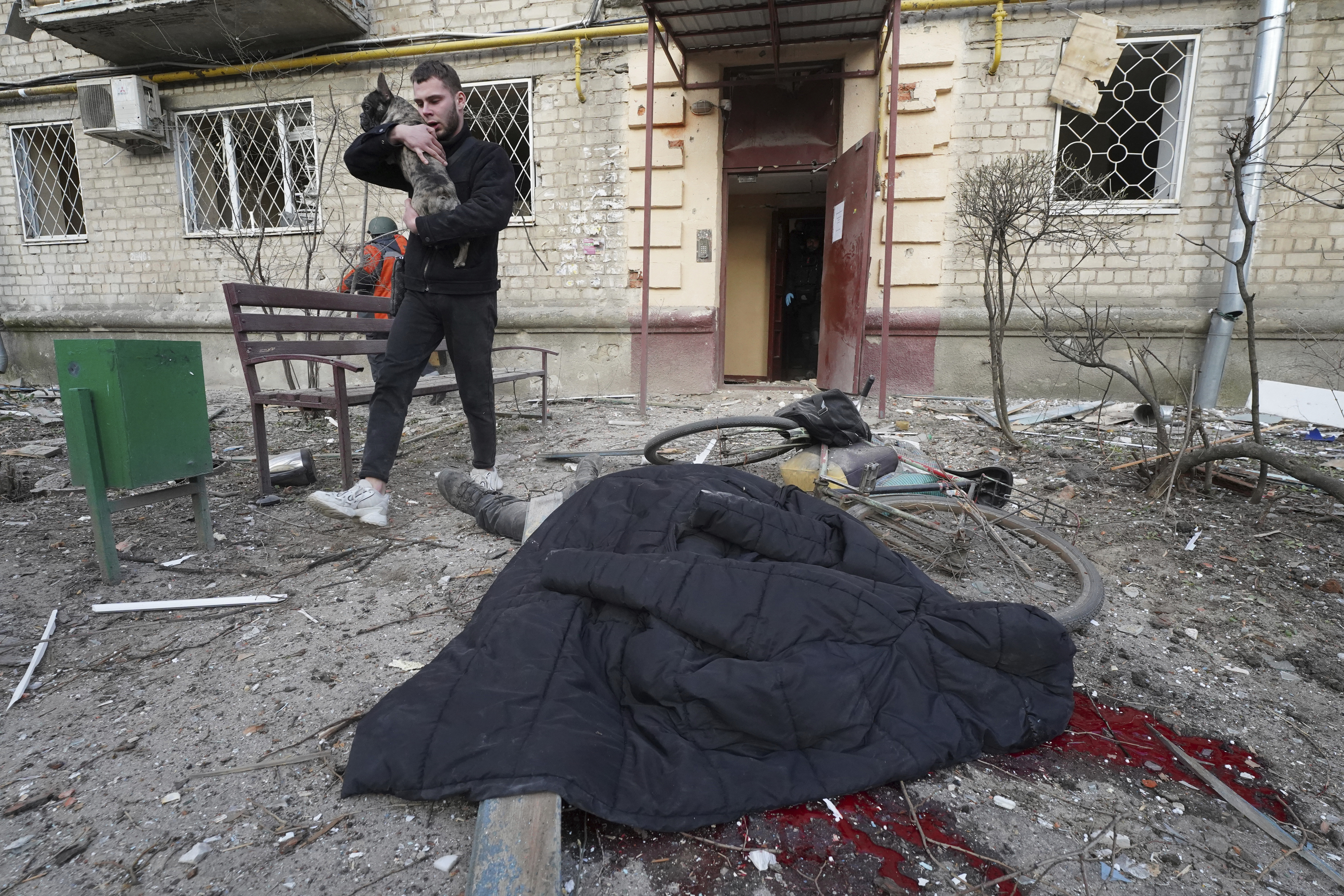 A man evacuates his dog while passing by a body of a man who was killed by a Russian strike in Kharkiv,