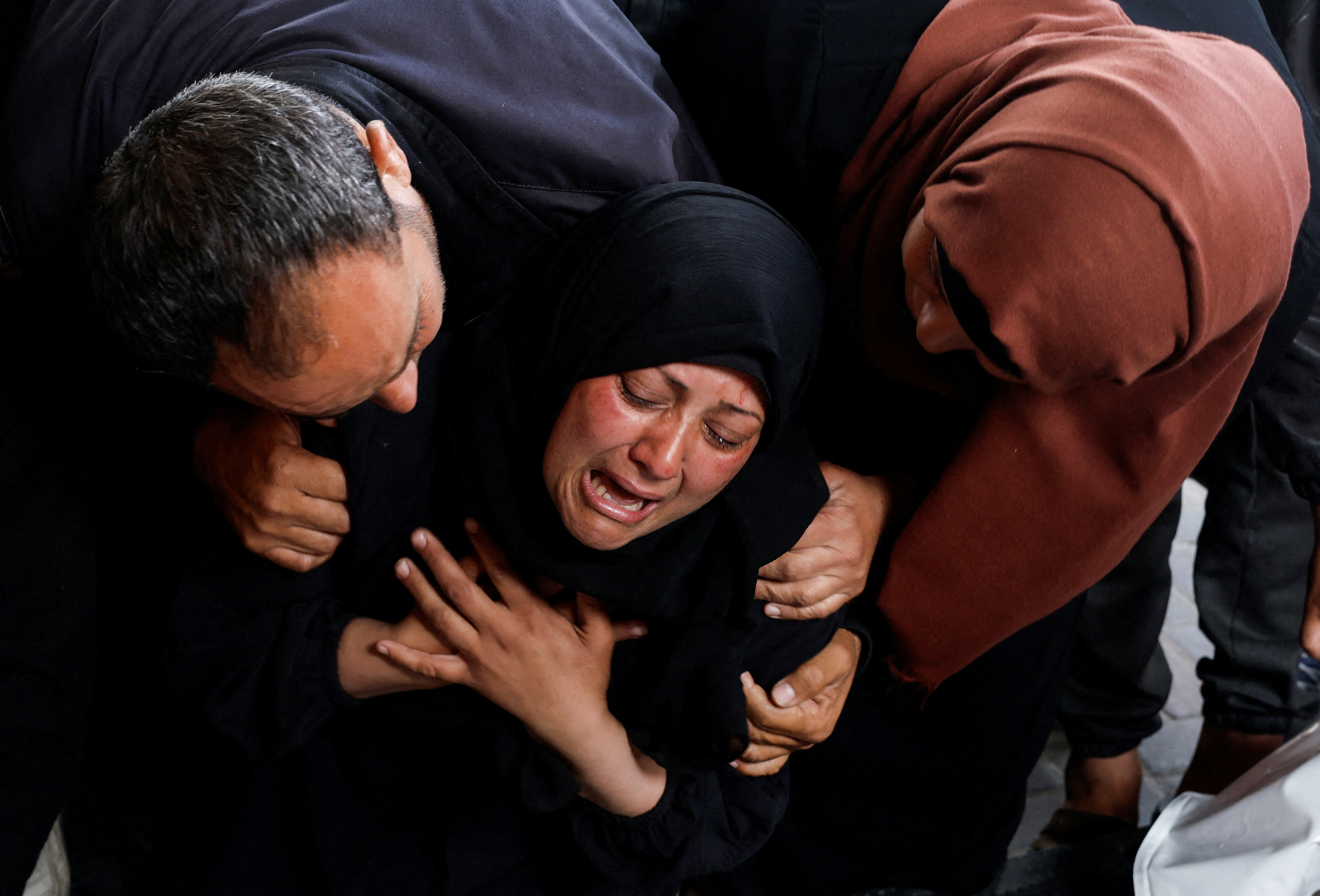people hold a woman as she mourns