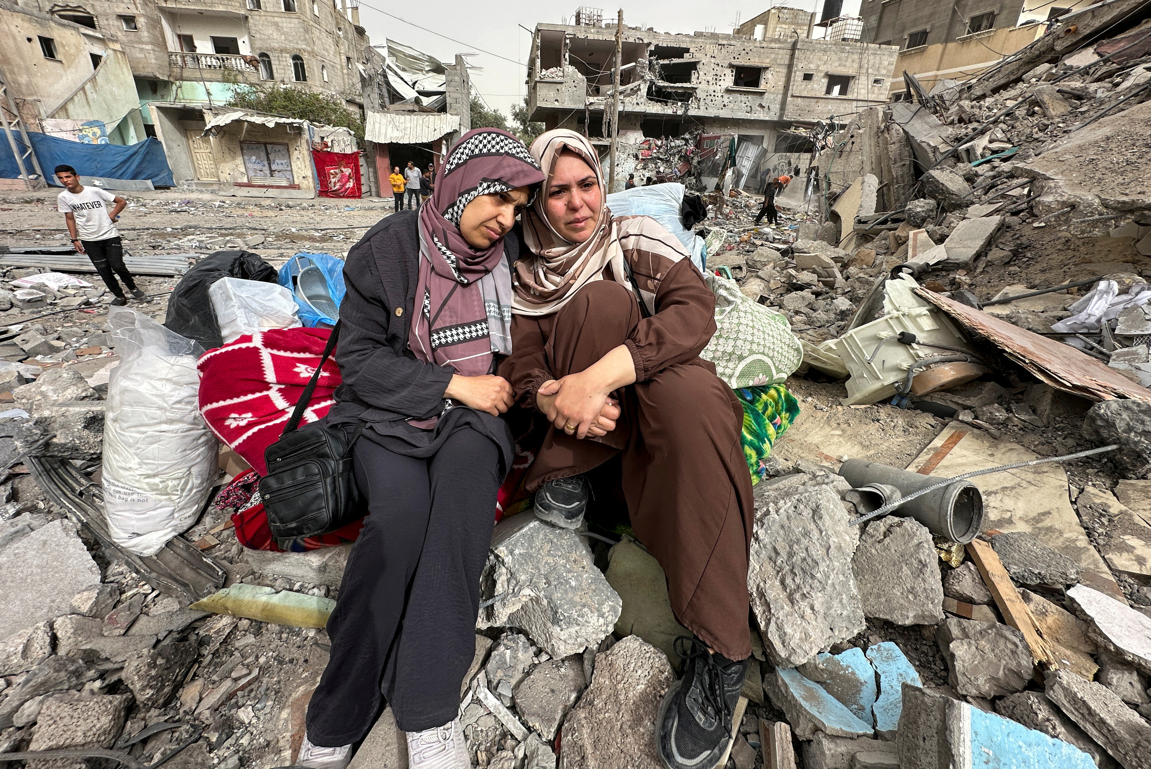 Palestinian women react as they sit on the rubble of a residential building housing their apartments, following an Israeli raid