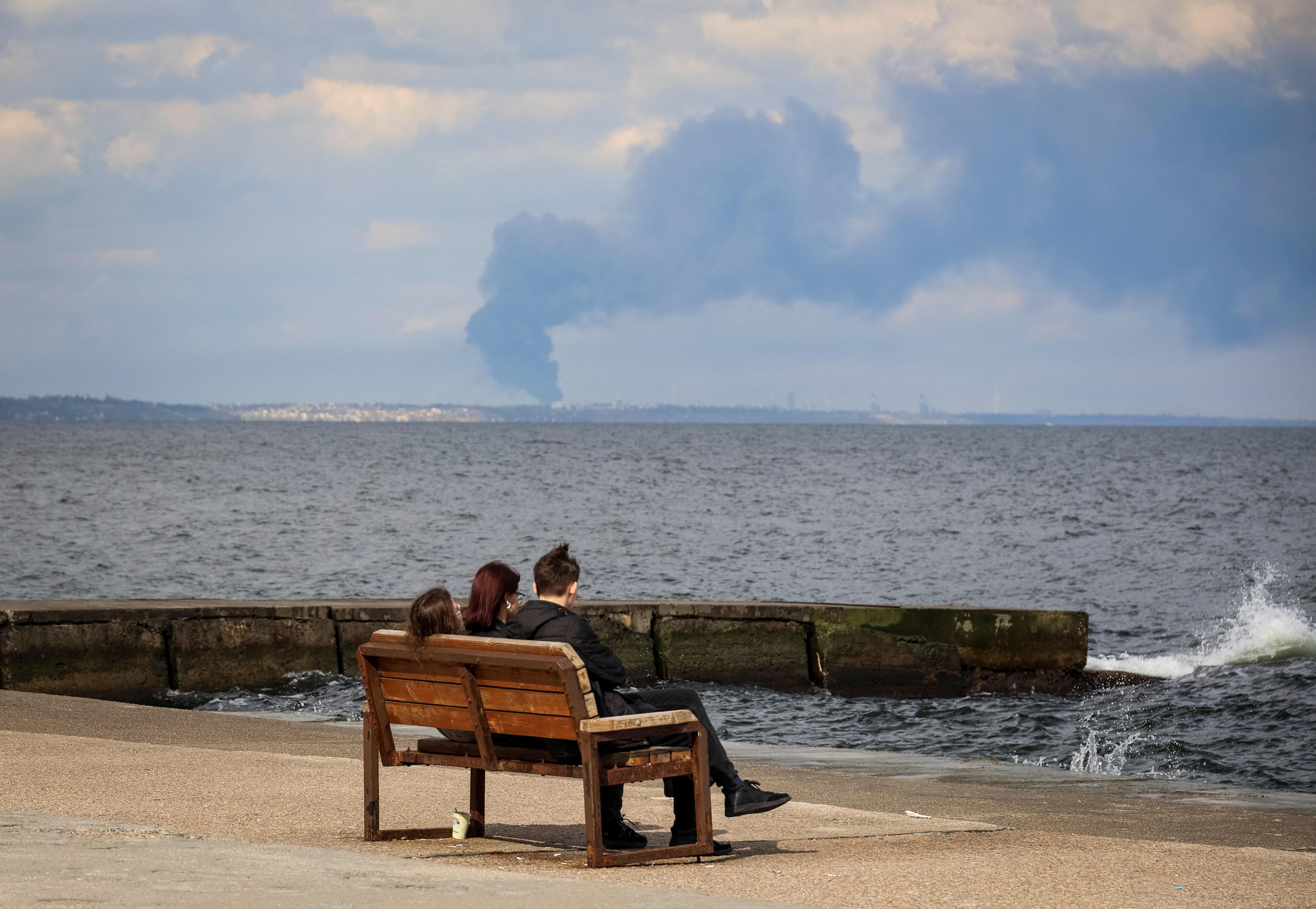 People rest on the beach as smoke rises over the port of Pivdennyi, after a Russian missile strike, amid Russia's attack on Ukraine, in Odesa, April 19, 2024. REUTERS/Nina Liashonok