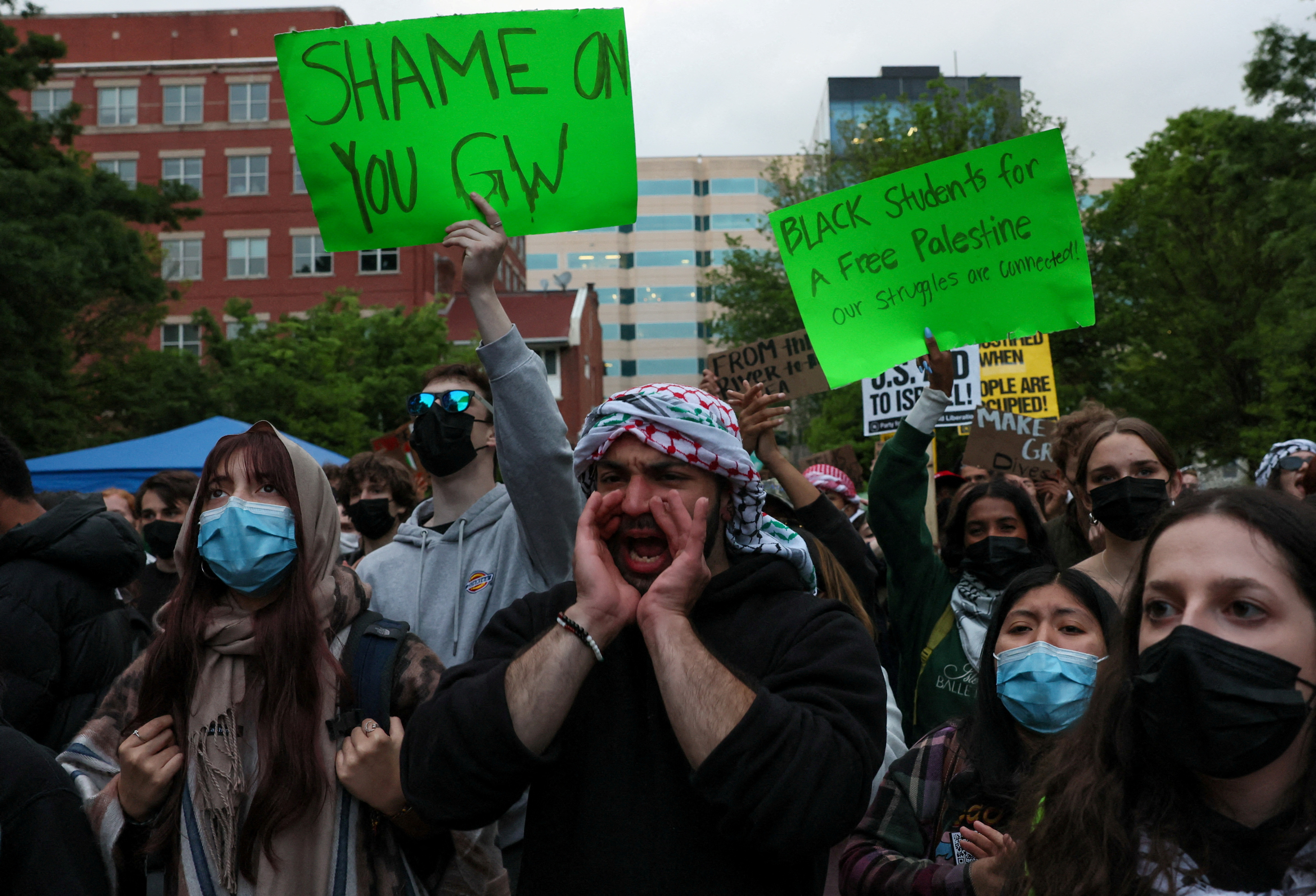 Students and others at a demonstration at George Washington University. One is carrying a banner reading 'Shame on you GW'. Another is carrying a placard reading 'Black students a free Palestine. Our struggles are connected' A man is shouting with his hands cupped around his mouth. Most are wearing face masks.