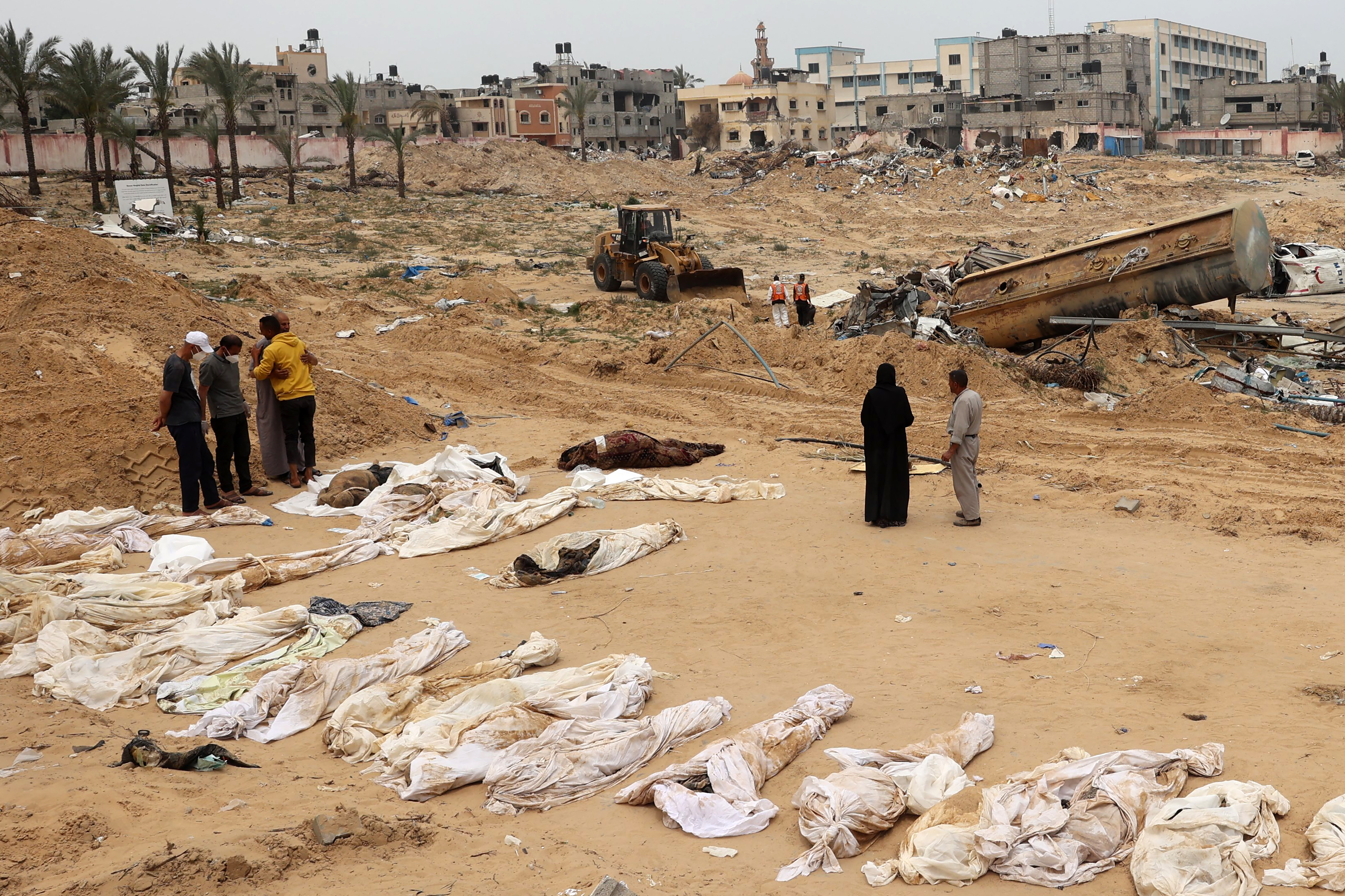 People gather near bodies lined up for identification after they were unearthed from a mass grave found in the Nasser Medical Complex in the southern Gaza Strip