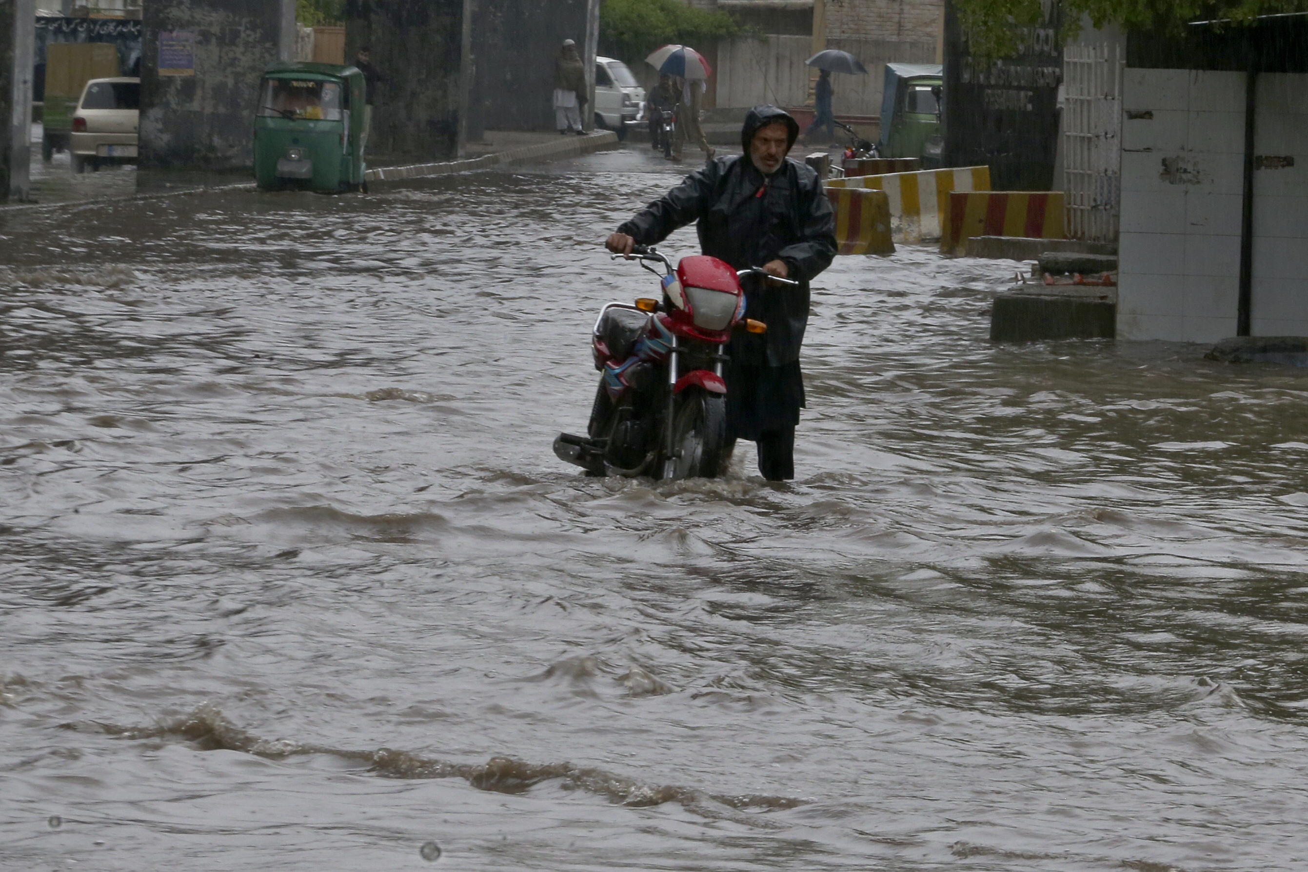A Pakistani with his bike wades through a flooded road caused by heavy rain in Peshawar, Pakistan, Monday, April 15, 2024. Lightening and heavy rains killed dozens of people, mostly farmers, across Pakistan in the past three days, officials said Monday, as authorities declared a state of emergency in the country's southwest following an overnight rainfall to avoid any further casualties and damages