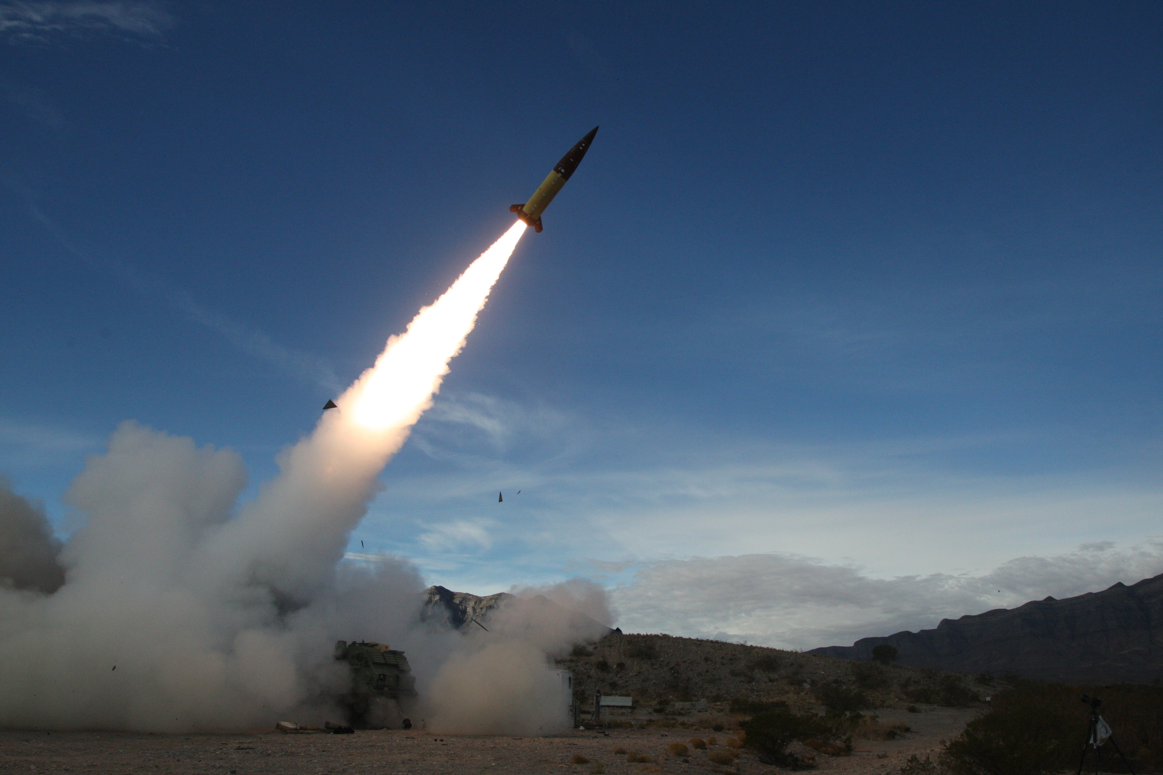 US soldiers conducting live fire testing of an ATACMS. The missile is taking off at an angle leaving a trail of fire and smoke.