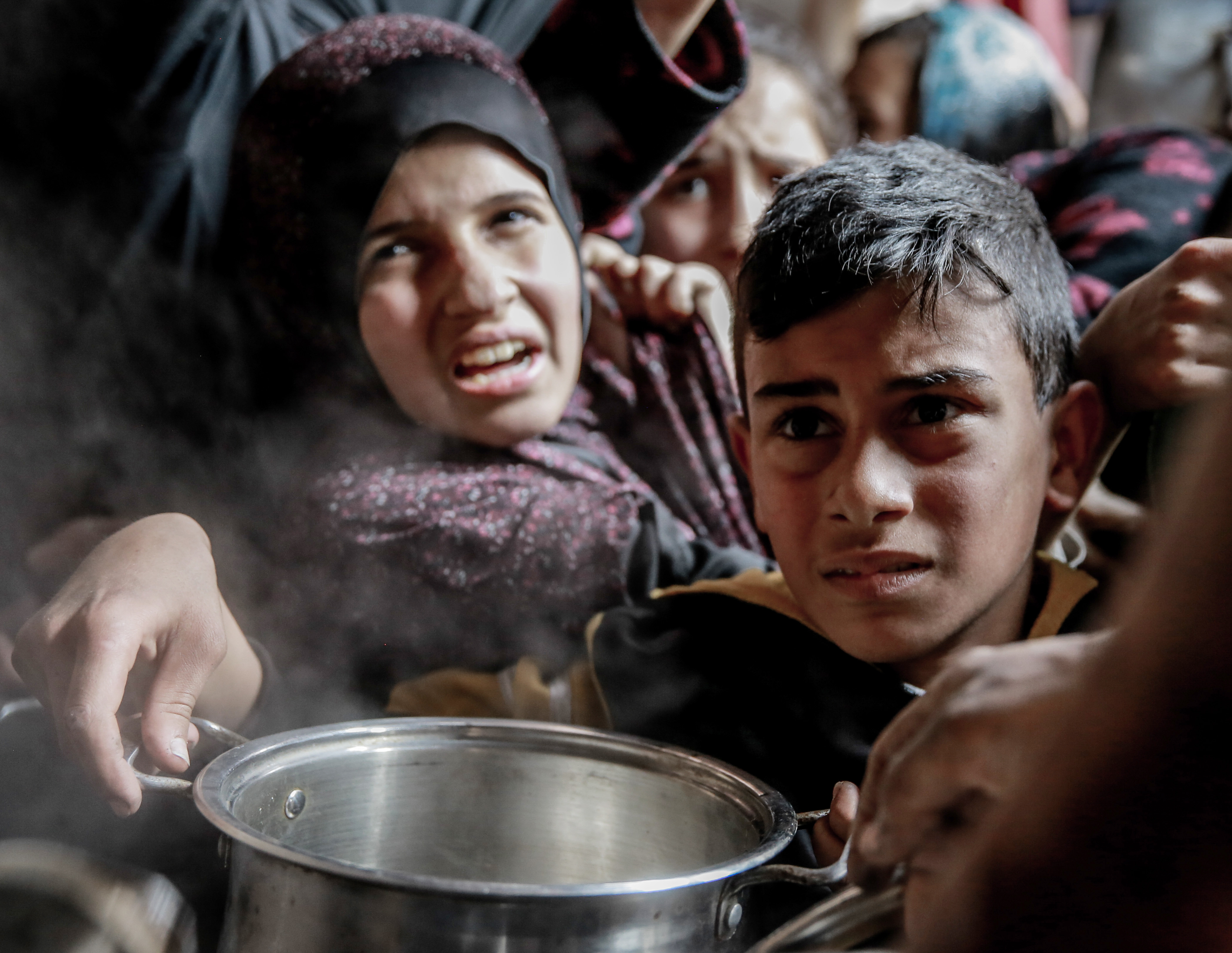 A child is seen holding an empty pan as he waits with others to receive hot food distributed by charitables and charity organization in Gaza City