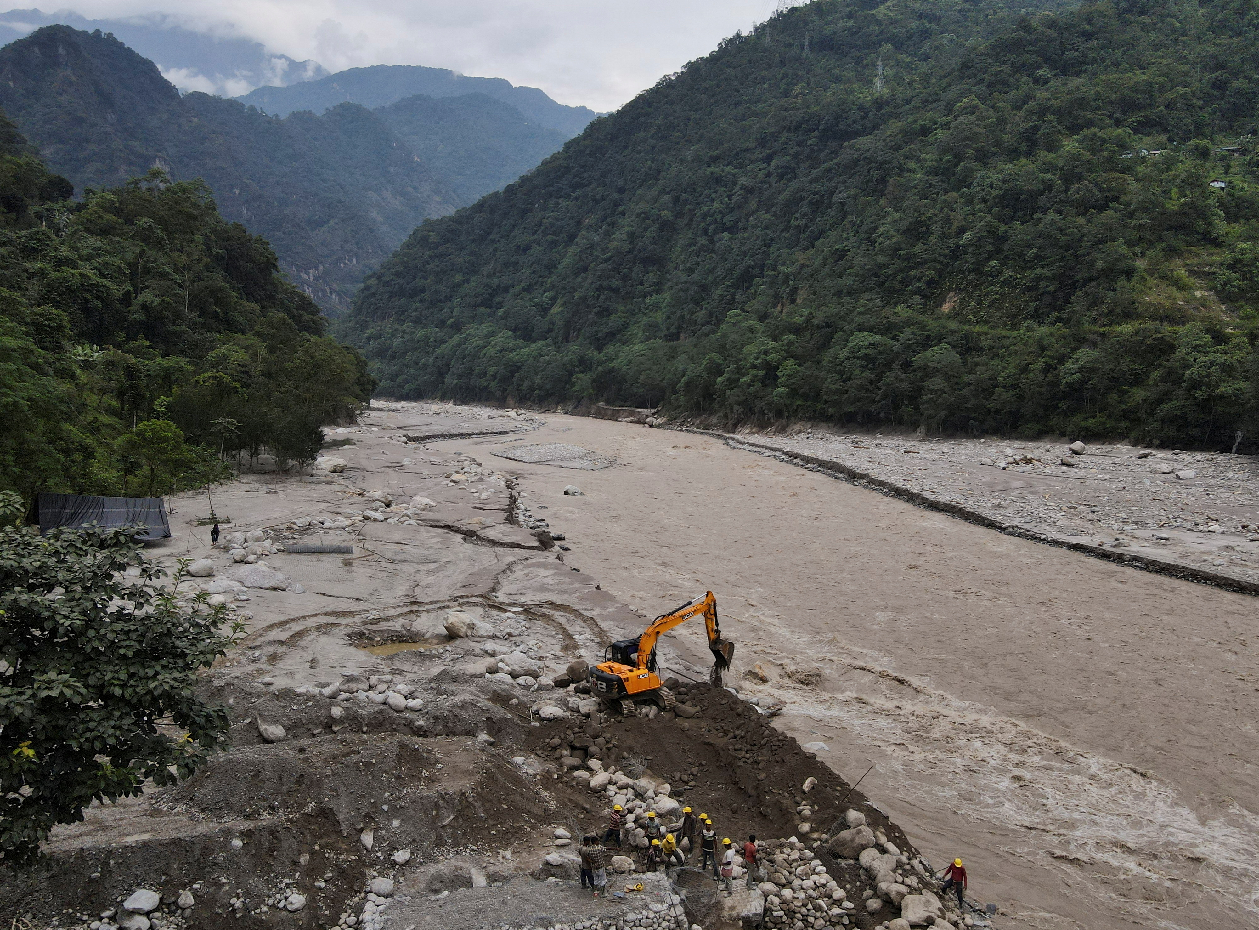 People and an excavator worki along the Teesta river to create a road to Dzongu village after flash floods washed away a bridge at Sangkalang, Sikkim, India