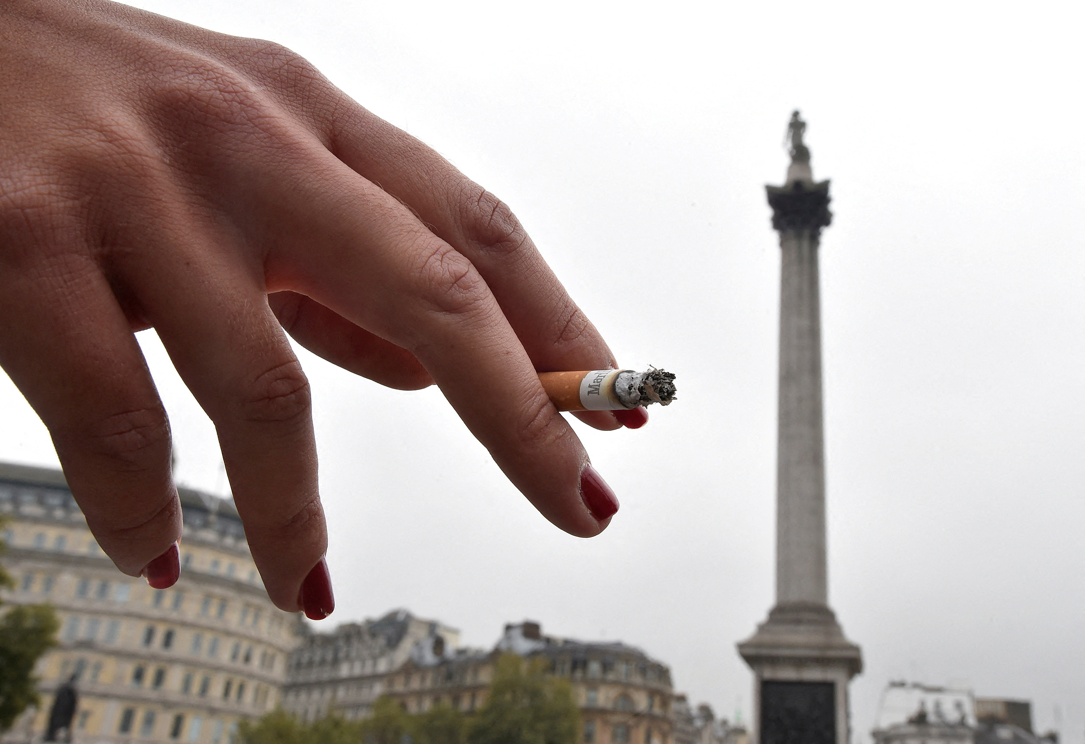 A woman holds her cigarette as she smokes in Trafalgar Square in central London
